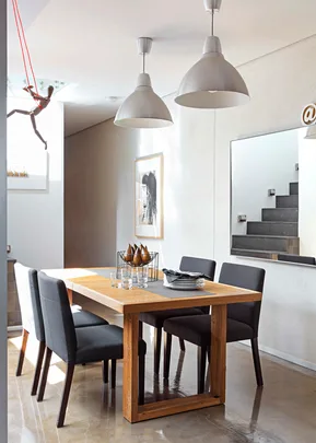 Modern dining room with wooden table, black chairs, pendant lights, wall art, and mannequin on red string.