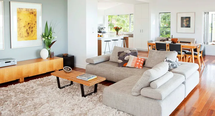 Modern living room with a grey sectional sofa, wooden coffee table, and dining area in the background.