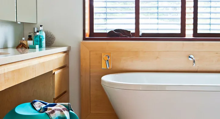 Modern bathroom with wooden accents, a freestanding tub, and toiletries on a countertop.