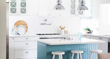 Modern kitchen with white cabinets, blue island, chrome lighting, and wooden stools.
