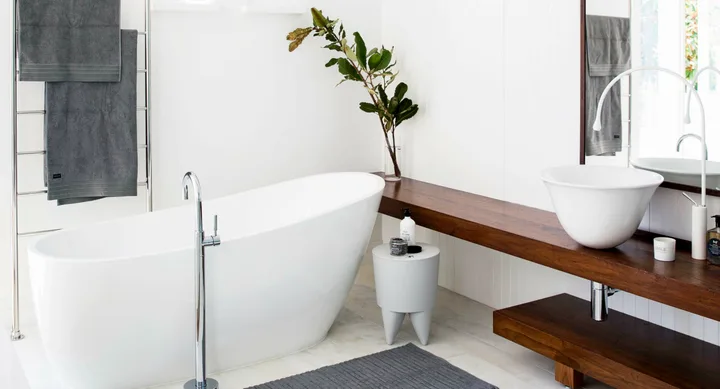 Modern bathroom with freestanding tub, vessel sink on wood counter, gray towels, and plant decor.