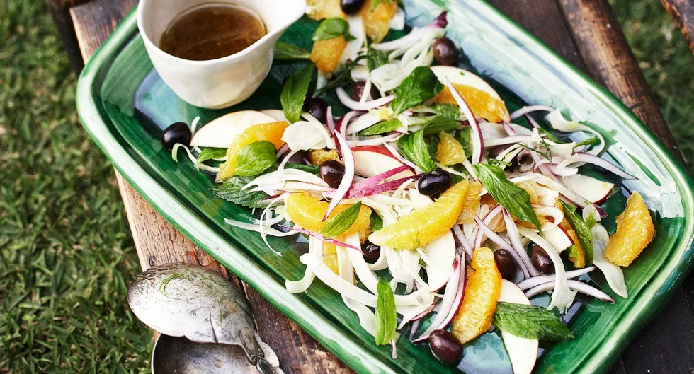 A green platter with fennel, orange, red onion salad with mint and olives, and a small bowl of dressing on the side.