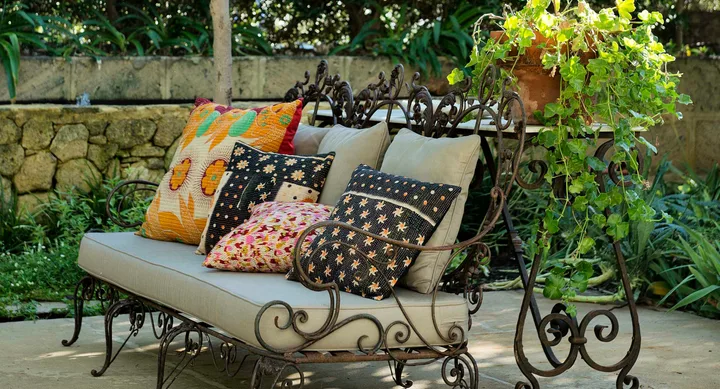 Outdoor metal bench with colorful cushions and nearby potted plant with green foliage on a patio.