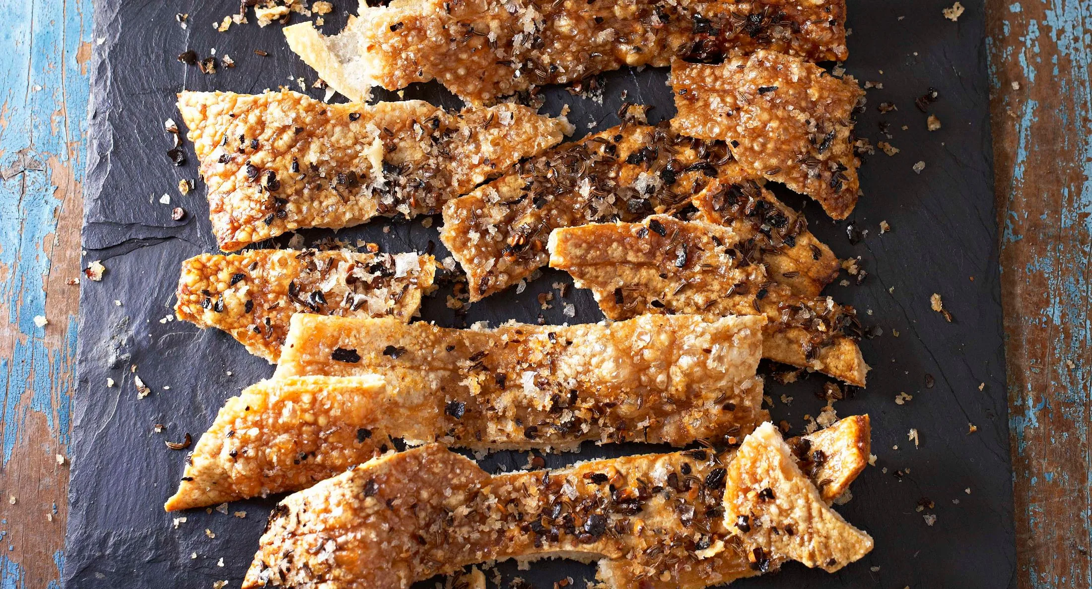 Crispy parmesan shards with black pepper and salt, arranged on a dark slate.
