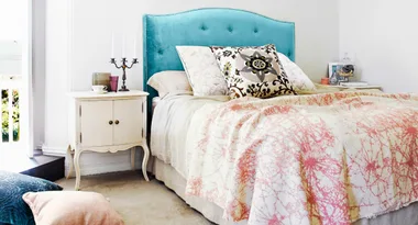 Elegant bedroom with a teal headboard, patterned pillows, and a white side table with decor items and candelabra.