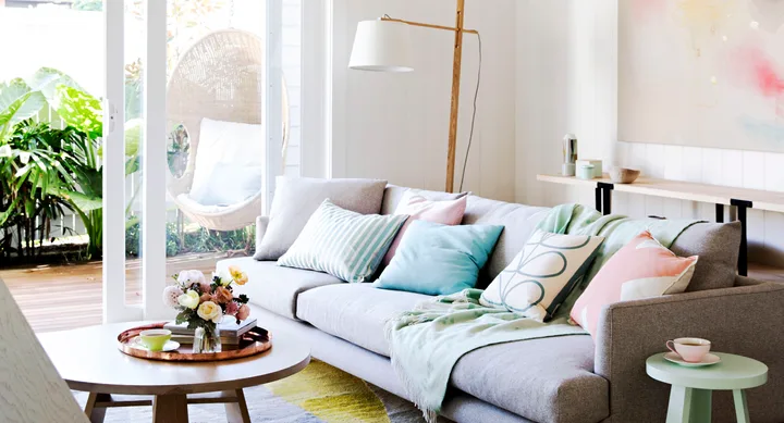 Bright, modern living room with a gray sofa, pastel cushions, a coffee table, and a hanging chair by a glass door.