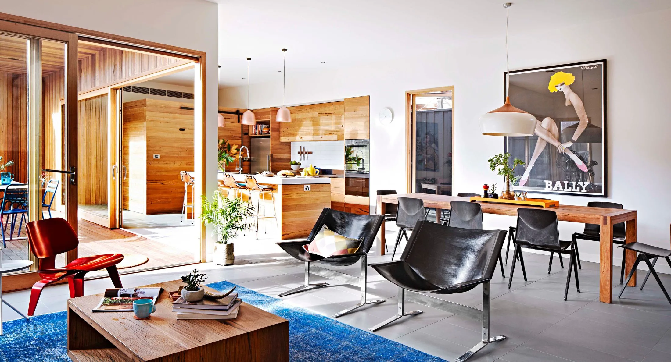 Open-plan living space with wood accents, modern furniture, colorful art on the wall, and large windows letting in sunlight.