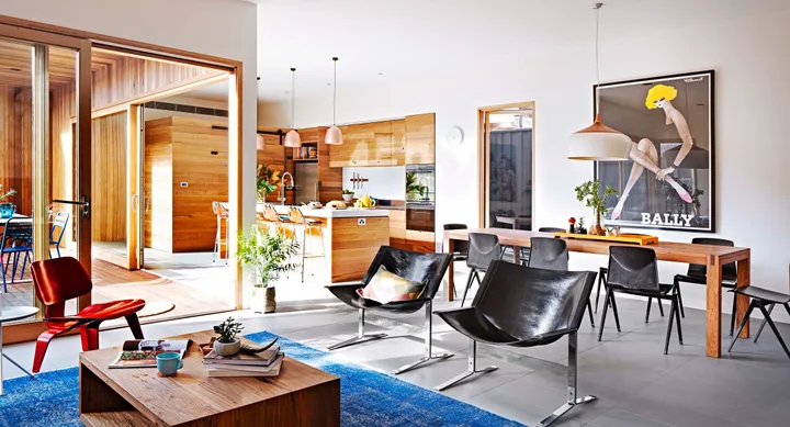 Open-plan living space with wood accents, modern furniture, colorful art on the wall, and large windows letting in sunlight.