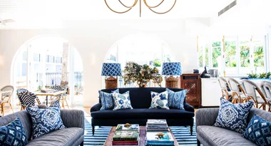 Coastal-themed living room with blue and white decor, striped rug, and wicker furniture.