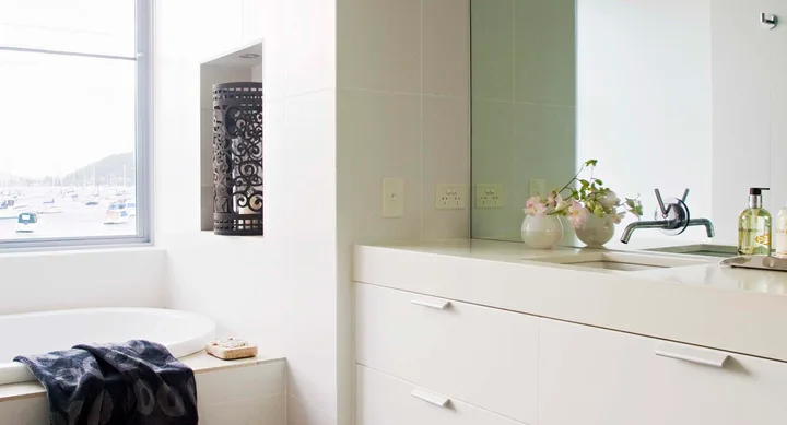 Modern bathroom with a white sink, flowers, faucet, and window view of sailboats on the water.