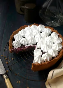 Berry pie with whipped topping, one slice missing, on a dark wooden table with a knife and napkin nearby.