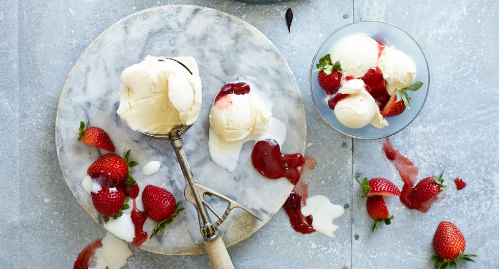 Ice cream scoops and strawberries on a marble surface with strawberry sauce drizzled around.