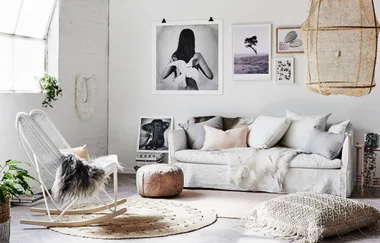 Cozy living room with white sofa, pastel pillows, a wicker chair, decorative wall art, and a large woven pendant light.