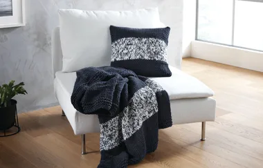 White chair with a knitted black and white pillow and a matching throw blanket draped over the side.