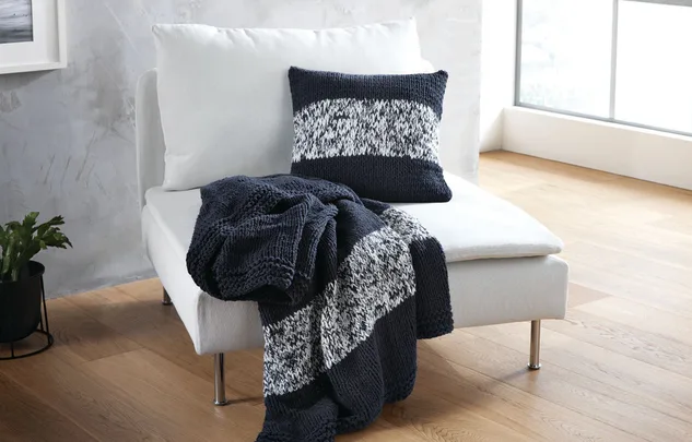 White chair with a knitted black and white pillow and a matching throw blanket draped over the side.