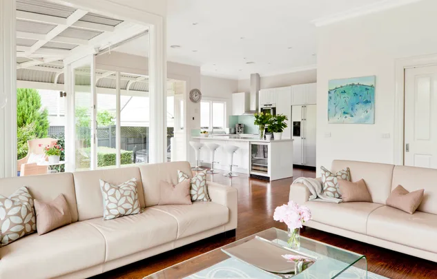 Modern open-plan living room and kitchen with beige sofas, cushions, white cabinetry, and glass doors to patio.