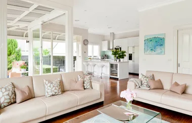 Modern open-plan living room and kitchen with beige sofas, cushions, white cabinetry, and glass doors to patio.