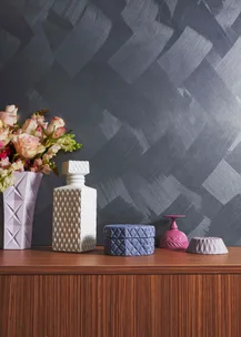 Decorative vases and jars with geometric designs on a wooden surface against a textured dark gray wall.