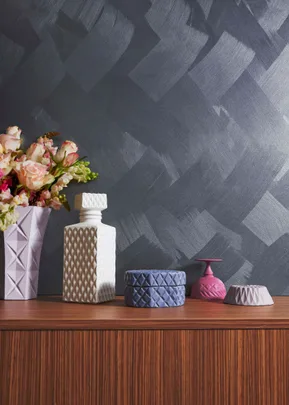Decorative vases and jars with geometric designs on a wooden surface against a textured dark gray wall.