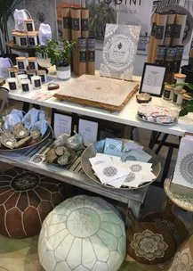 Display of Yogini products including mandala stencils, candles, textiles, and decorative items on a table.