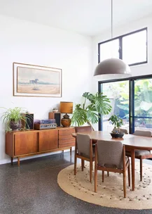 Mid-century modern dining room with wooden furniture, plants, and a large window.
