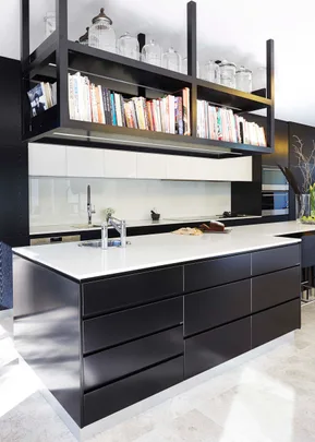 Modern kitchen with a black island, white countertop, overhead bookshelf, and glass jars.