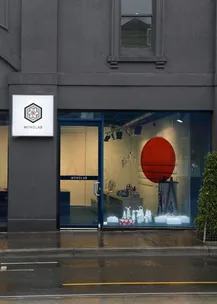 Storefront of Monolab with glass door, modern logo, and art display visible from the street on a rainy day.