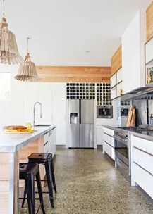 Modern kitchen with wooden accents, pendant lights, marble countertops, steel appliances, and a wine rack.