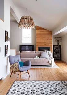 Living room with a modern brown sofa, patterned armchair, wooden chandelier, and geometric rug on hardwood floor.