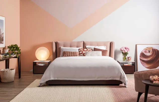 Modern bedroom with a pastel peach accent wall, a plush bed, side tables, and decorative elements like plants and art.