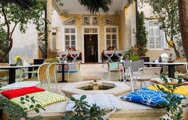 Outdoor cafe with colorful cushions, tables, and chairs in a cozy courtyard setting with plants and potted flowers.