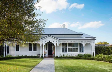 A charming white Victorian-style house with ornate trim, front porch, and manicured lawn under a clear blue sky.