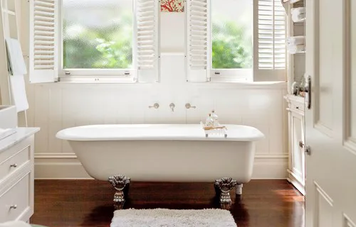 Alt text: Elegant bathroom with clawfoot tub, wooden floors, and white shutters on windows for natural light.