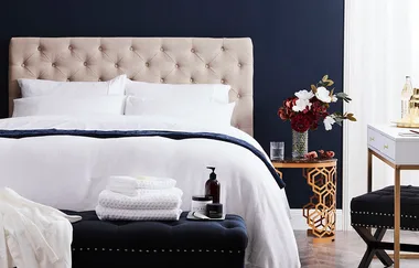 Luxurious bedroom with beige tufted headboard, white bedding, and a decorative side table with flowers.