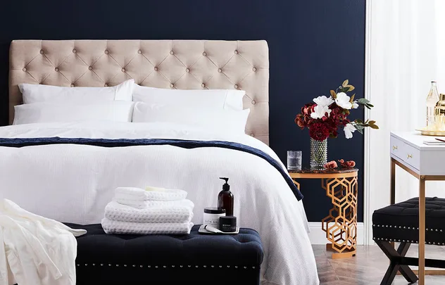 Luxurious bedroom with beige tufted headboard, white bedding, and a decorative side table with flowers.