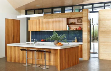 Modern kitchen with wooden cabinets, large island, three stools, and decorative items like plants and fruit basket.