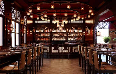 Elegant bar with dim lighting, bottles on shelves, round ceiling lights, and table settings in a vintage ambiance.