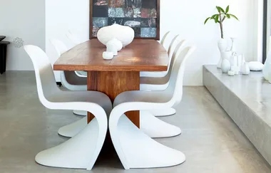 Modern dining room with a wooden table, six white chairs, abstract art on the wall, and minimalist decor.