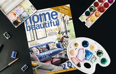 Cover of "Home Beautiful" magazine on a table with watercolor paints and a palette.