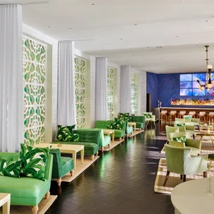Contemporary lounge with green seating, white patterned walls, and a bar. Elegant decor and modern lighting.