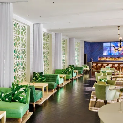 Contemporary lounge with green seating, white patterned walls, and a bar. Elegant decor and modern lighting.