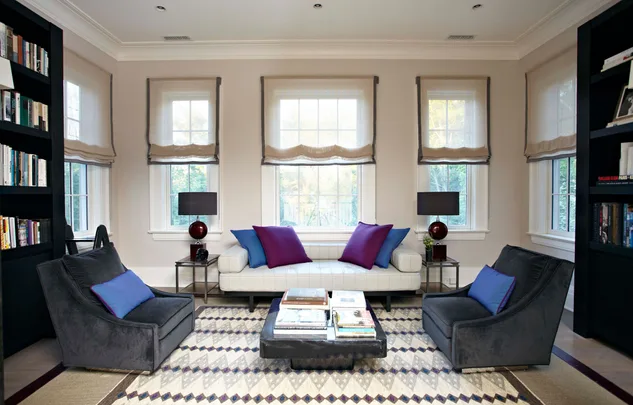 Modern living room with white sofa, colorful pillows, gray chairs, bookshelves, and a patterned rug.