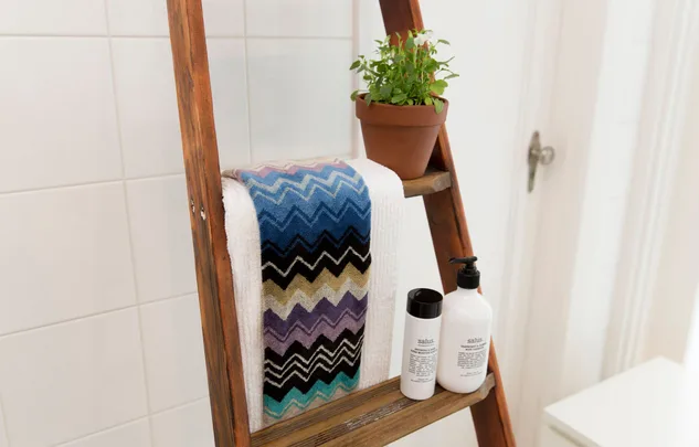 Towel rack with zigzag towel, potted plant, and toiletries on wooden ladder shelf in a bathroom setting.