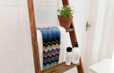 Towel rack with zigzag towel, potted plant, and toiletries on wooden ladder shelf in a bathroom setting.