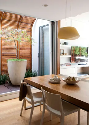 Contemporary dining area with wooden table, white chairs, a potted plant, and a modern TV unit.