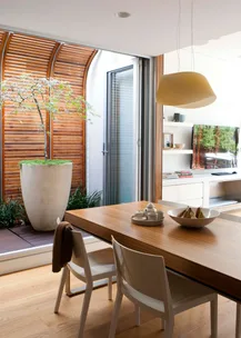 Contemporary dining area with wooden table, white chairs, a potted plant, and a modern TV unit.