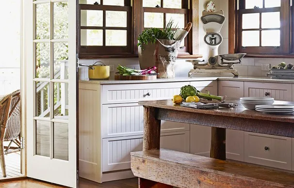 Rustic kitchen with wooden counter, vintage scale, white cabinets, and fresh produce near a sunny window.