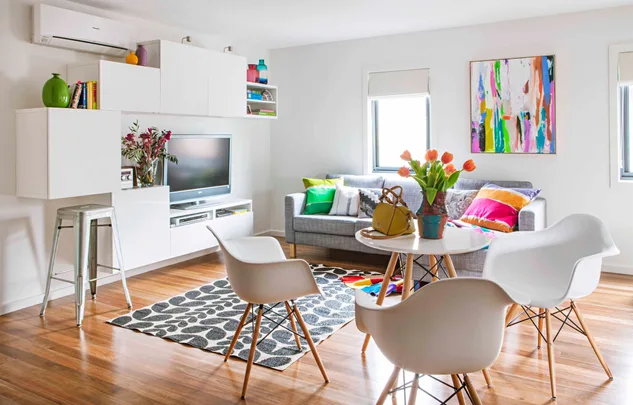 Bright living room with modern furniture, colorful cushions, abstract art, and flowers on a round table.