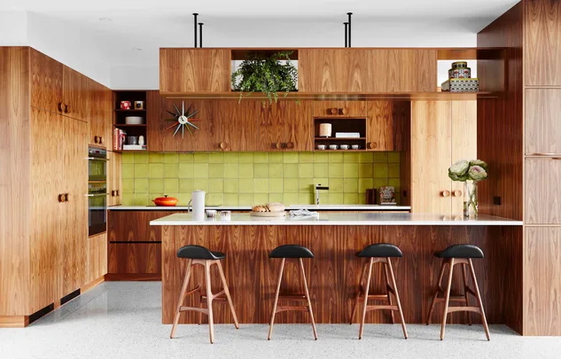 Mid-century modern timber and green kitchen with wooden cabinets, green tile backsplash, and a white island with four stools.
