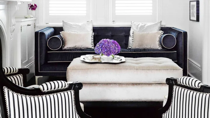 Elegant living room with black sofa, striped chairs, and a ceiling light. Purple flowers in a vase on the coffee table.